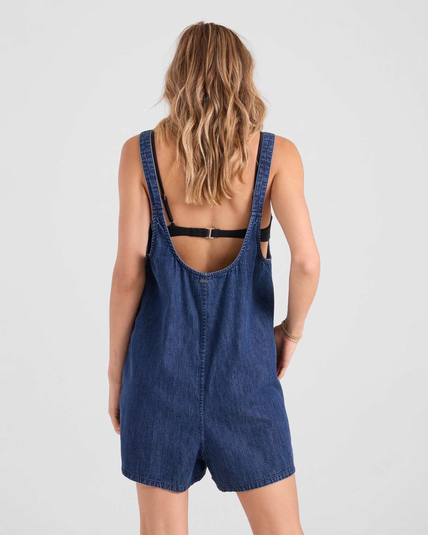 Back view of woman wearing Volcom denim short romper with overall straps