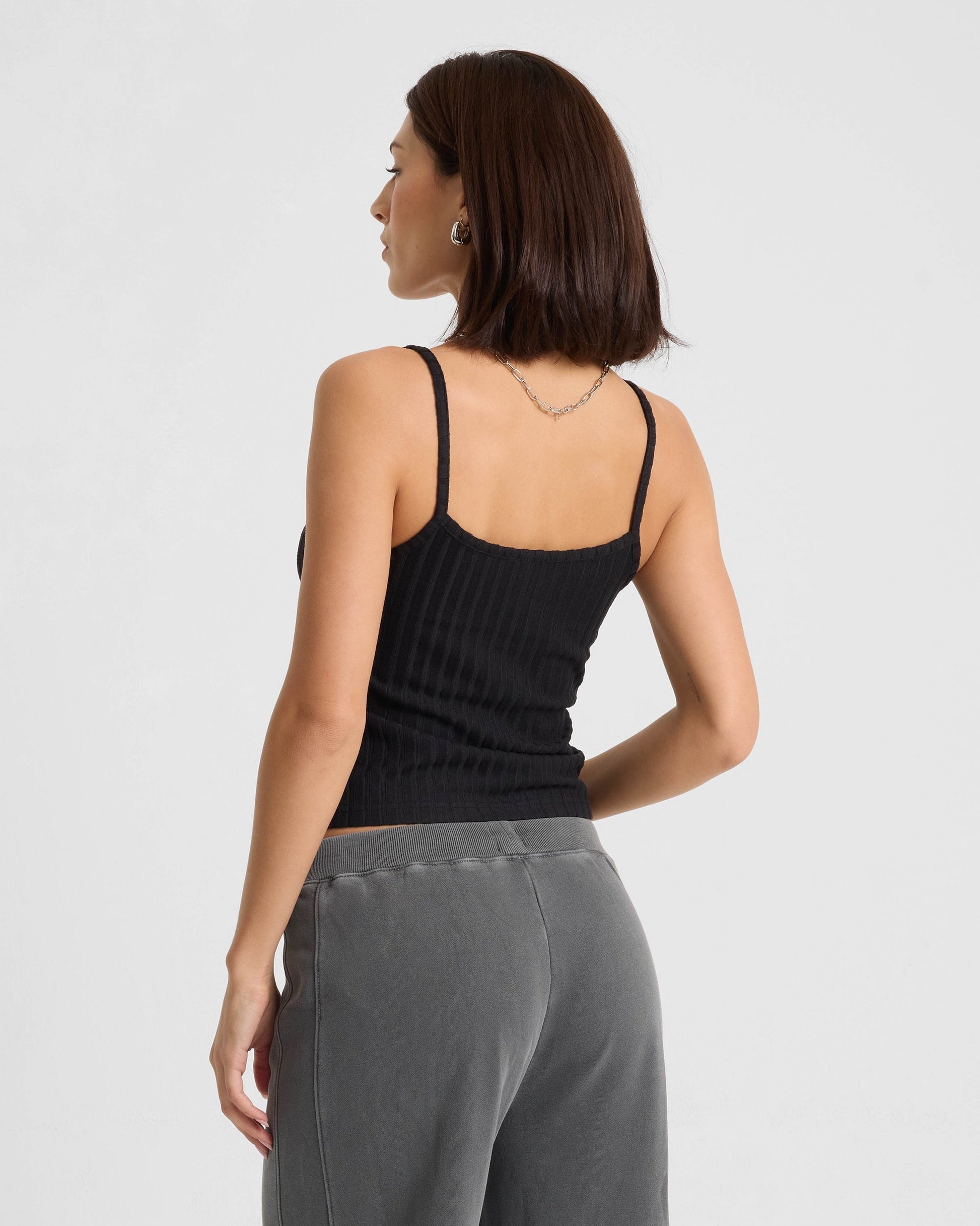 Woman wearing black ribbed tank top with gray sweatpants, back view studio shot