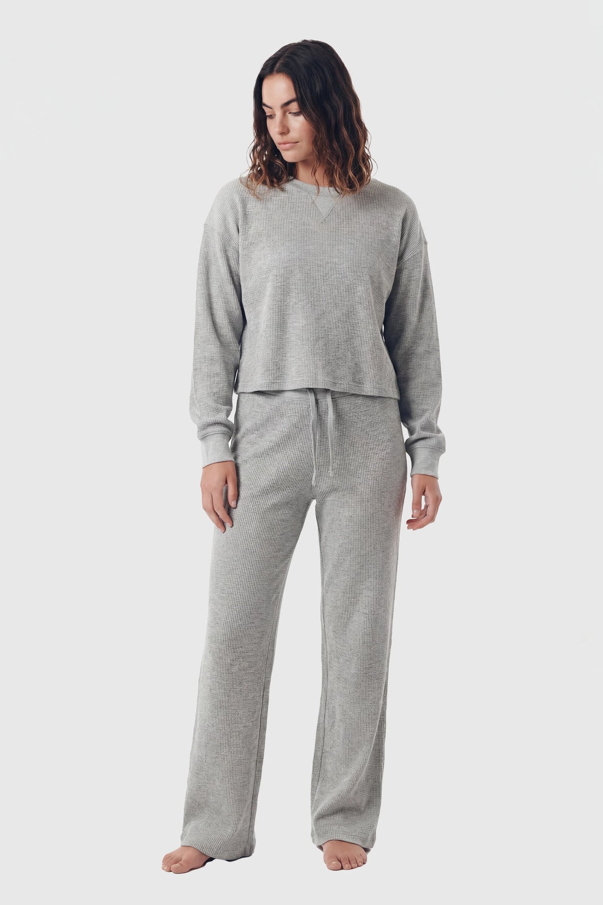 Woman wearing grey waffle-knit lounge pants and matching crewneck top on white background