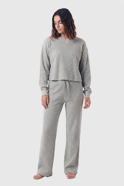 Woman wearing grey waffle-knit lounge pants and matching crewneck top on white background