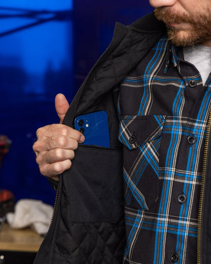 Man opening black Dixxon Outlaw Work Vest revealing interior phone pocket with blue iPhone