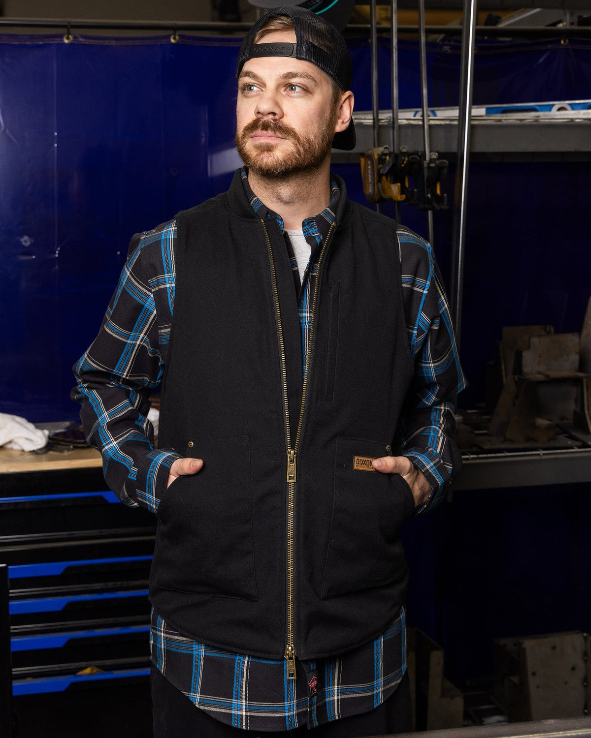 Dixxon Outlaw Work Vest in black with gold zipper worn over blue plaid flannel shirt